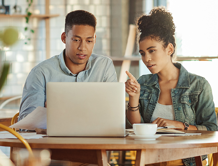 Two business partners sitting in a café looking at their computers.